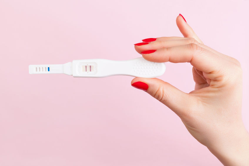 beautiful female hand with red fingernails holding positive pregnancy test isolated on pink background. motherhood, pregnancy, birth control concept. minimal sparse modern image language.
